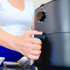Dłoń osoby wyciąga szufladę frytkownicy beztłuszczowej, pokazując, jak działa air fryer.