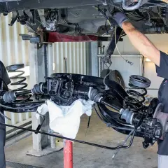 Mechanicy pracują nad zarabianiem przewodów hamulcowych przy podniesionym zawieszeniu samochodu.