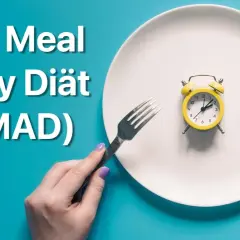 Ein Teller mit einem Wecker symbolisiert die "One Meal a Day Diät" (OMAD). Gabel und Messer warten auf die einzige Mahlzeit des Tages.
