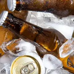 Chłodne piwo w butelkach i puszkach wśród kostek lodu. Szukasz piwa alkoholowego, które ma najmniej kcal?