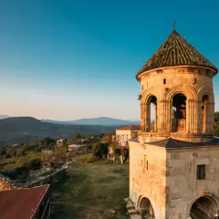 Wieża dzwonnicza Gelati Monastery na tle górskiego krajobrazu o zachodzie słońca.
