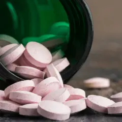 Różowe tabletki wysypują się z zielonego pojemnika. Wśród nich widać tabletki z chromem, które mogą pomóc w utrzymaniu prawidłowego metabolizmu.