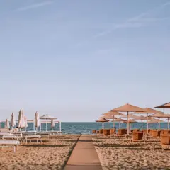 Ombrelloni e lettini pronti per accogliere i bagnanti sulla riviera romagnola, con il mare calmo all'orizzonte.