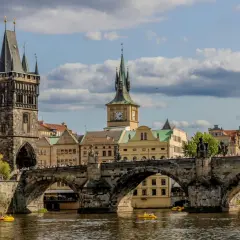 Most piękne stolice Europy, Most Karola w Pradze, z wieżami i zegarem, na tle błękitnego nieba z chmurami.
