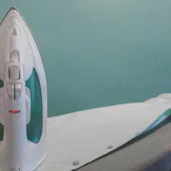 Fer à repasser blanc sur une planche, prêt à enlever colle sur chemise.