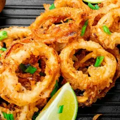 Crujientes calamares en salsa, adornados con cebolleta y lima, listos para disfrutar.