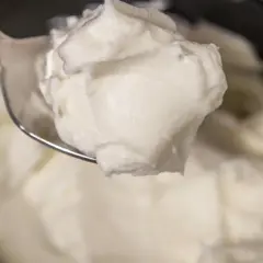 Un cucchiaio raccoglie una generosa porzione di cremoso yogurt greco fatto in casa, pronto per essere gustato.
