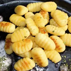 Złociste, domowe **makaron gnocchi** z ziołami, ułożone na ciemnym talerzu.
