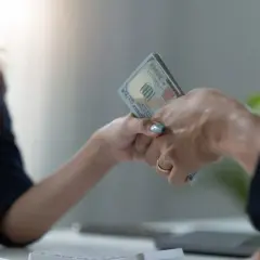 Dwie osoby przekazują sobie plik banknotów. To może być pożyczka od osoby prywatnej, która pomoże w nagłej potrzebie.