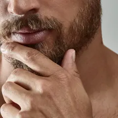 Gros plan sur un homme pensif, sa main caressant sa barbe. L'évolution de sa barbe, de la naissance à sa forme actuelle, est visible.