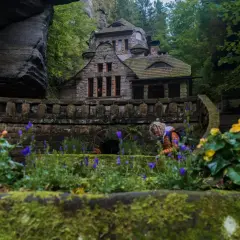 Kamienny domek w sercu Szwajcarii Czeskiej, otoczony bujną zielenią i kwitnącymi kwiatami.