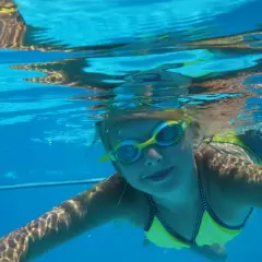 Enfant souriant sous l'eau, lunettes de piscine, maillot jaune. Attention à l'otite de piscine après ces moments joyeux.