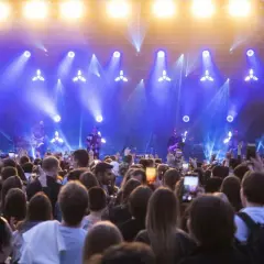 Tłumy bawią się na koncercie podczas juwenaliów WUM. Artyści grają na scenie oświetlonej niebieskimi światłami.