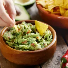 Ręka zanurza chipsa w misce z guacamole. To pyszne, zielone danie, idealne do nachos.