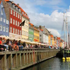Bunte Häuser am Nyhavn, Kopenhagen an einem Tag. Menschen sitzen am Kai, Boote liegen im Wasser.