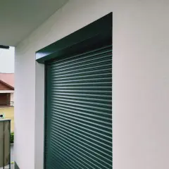 Zacięta roleta wewnętrzna czeka na naprawę. W tle dom z czerwonym dachem.