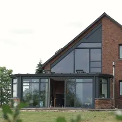 Nowoczesny dom z cegły z dużymi, przeszklonymi oknami w ścianie szczytowej i oranżerią.