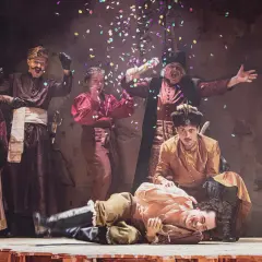 Aktorzy w strojach ludowych świętują na scenie, sypiąc konfetti. To fragment repertuaru teatru ludowego.