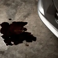 Mancha oscura de aceite en el suelo de hormigón, indicando una **pérdida de aceite del coche**.