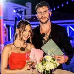 Para z Love Island, która wygrała, pozuje z uśmiechem. Ona w czerwonej sukience, on w czarnym garniturze.