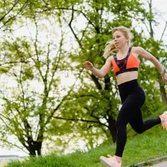 Młoda kobieta w sportowym stroju biegnie po ścieżce w parku. To świetny przykład na bieganie dla początkujących, pełne energii i radości.