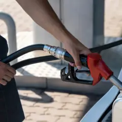 Osoba nalewa paliwo z dystrybutora do kanistra w bagażniku samochodu.