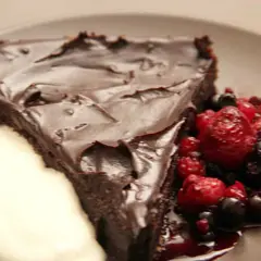 En bit chokladkaka med tryffel, toppad med mörk chokladglasyr, serveras med färska bär och en klick grädde.
