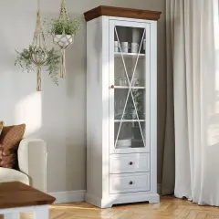 Biała witryna z drewnianym blatem, idealna do salonu. W środku szkło i zastawa, na dole szuflady. Wiszące makramy z roślinami dodają uroku.