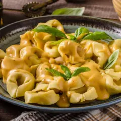 Plato de tortellini de carne cubiertos con una cremosa salsa de queso y decorados con hojas de albahaca fresca.