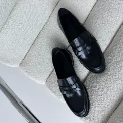 Eleganckie, czarne, lakierowane mokasyny leżą na białym, teksturowanym fotelu. Idealne, by dowiedzieć się, jak zmiękczyć skórzane buty.