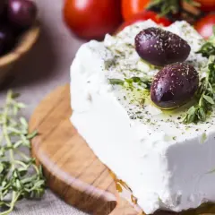 Kostka sera feta, polana oliwą i posypana ziołami, z oliwkami i pomidorkami w tle. Właściwości sera feta doceniane są w kuchni śródziemnomorskiej.