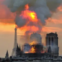 Płonąca katedra Notre-Dame w Paryżu z Wieżą Eiffla w tle.