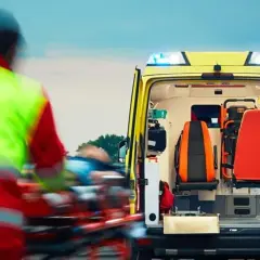 Ratownik medyczny w kamizelce odblaskowej transportuje pacjenta do karetki.