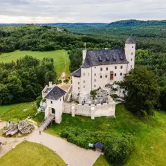 Malowniczy zamek Bobolice, wzniesiony na skale, otoczony zielonymi lasami i polami.