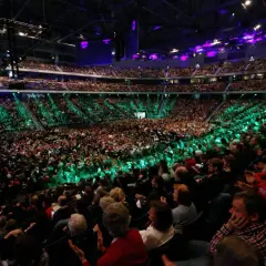 Tausende Menschen in einer Arena, beleuchtet von grünen und violetten Lichtern. Eine beeindruckende Kulisse für eine mega church Veranstaltung.
