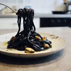 Pâtes noires, colorées avec de l'encre de seiche, c'est quoi ce plat savoureux ? Elles sont servies avec des moules sur une assiette.