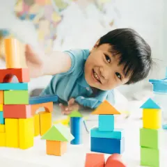 Niño sonriente jugando con bloques de colores, creando torres y casas. Perfectos juegos niños 3 años en casa para la imaginación.
