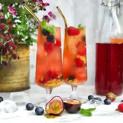 Två glas med fruktiga drinkar, fyllda med bär och passionsfrukt. Perfekt för en somrig bål med bubbel.