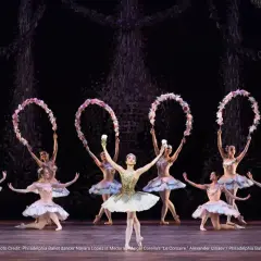 Balettdansöser i ljusa dräkter utför en scen från "Le Corsaire", med blomsterkransar i händerna.