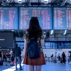 Kobieta z plecakiem patrzy na tablicę odlotów, szukając swojego numeru pnr.