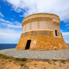Torre de defensa costera, un lugar histórico que ver en Fornells. El mar azul y el cielo nublado completan la vista.