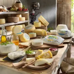 Un ricco elenco formaggi italiani, tra cui freschi e stagionati, disposti su un tavolo di legno con miele, olio e marmellata.