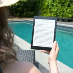 Une personne lit un epub en ligne au bord d'une piscine, profitant du soleil et d'une lecture immersive.