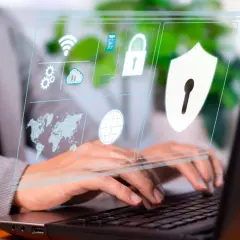 Osoba pracuje przy laptopie, a na ekranie wyświetla się interfejs z ikonami symbolizującymi cyberbezpieczeństwo: globus, mapa świata, chmura, kłódka i tarcza.