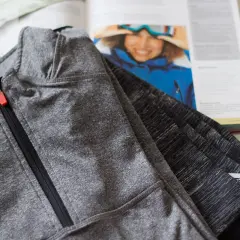 Szara bluza sportowa z zamkiem, wykonana z poliamidu, leży obok otwartej książki z narciarką.