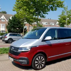 Dwukolorowy volkswagen van, czerwono-srebrny, zaparkowany na tle domów i drzew.