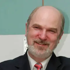 Ein Mann mit Glatze und Bart, Thomas Schirrmacher, lächelt in die Kamera. Er trägt einen dunklen Anzug und eine Krawatte.