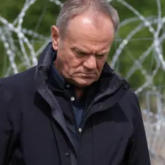 Mężczyzna w ciemnej kurtce patrzy w dół, za nim drut kolczasty. Czy to symbol jego hipokryzji?