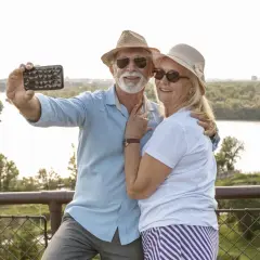 Uśmiechnięta para seniorów robi selfie na tle rzeki. Idealne wycieczki dla seniorów samolotem to świetny sposób na podróżowanie.