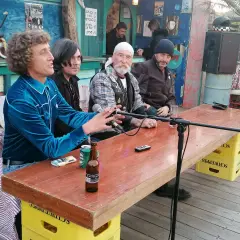 Hombres sentados en una mesa de madera en el bar de Joe Cabo de Gata, con micrófonos y botellas de cerveza.